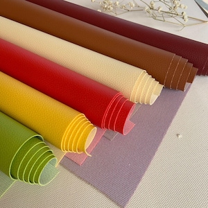 May include: A collection of rolled-up sheets of textured faux leather in various colors. The colors include shades of green, yellow, red, cream, brown, and burgundy. The sheets are arranged diagonally, showcasing their different hues and textures.