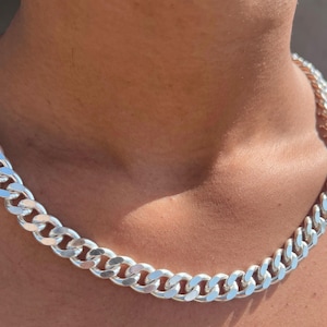 May include: A silver curb chain necklace. The necklace is made of interlocking links and is worn around the neck. The chain has a shiny, reflective surface.