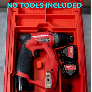 Op de afbeelding: Rode en zwarte draadloze schroefboorset in een rode koffer. De schroefboormachine is van het merk Milwaukee. De koffer heeft de tekst "NO TOOLS INCLUDED" in het blauw. De set bevat de schroefboormachine en twee batterijen.
