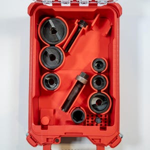 May include: A red tool case with a clear lid, filled with various black and silver metal tools. The tools include circular punch dies and bolts, neatly organized within the case. The case is designed for tool storage and organization.