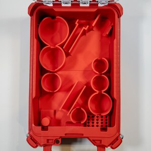May include: Open red plastic toolbox with various compartments and molded shapes. The interior features circular and rectangular spaces, along with angled slots. The toolbox is designed for organizing tools and accessories.