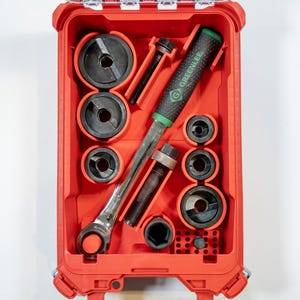 May include: A red tool case containing various tools, including a ratchet, sockets, and a Greenlee branded tool. The tools are black and silver, with a green handle on one tool. The case is rectangular and has a hinged lid.