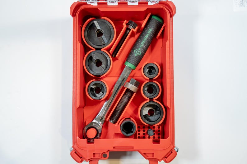 May include: A red tool case containing various tools, including a ratchet, sockets, and a Greenlee branded tool. The tools are black and silver, with a green handle on one tool. The case is rectangular and has a hinged lid.