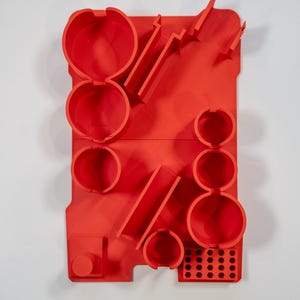 May include: A vibrant red wall organizer with various circular and rectangular compartments. The organizer features multiple cylindrical holders, angled slots, and a grid of small holes. The design is modern and geometric, with a solid, matte finish.