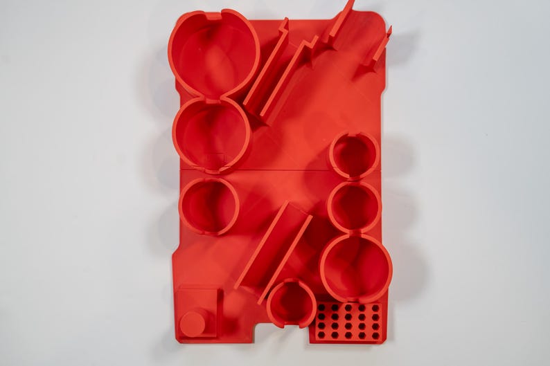 May include: A vibrant red wall organizer with various circular and rectangular compartments. The organizer features multiple cylindrical holders, angled slots, and a grid of small holes. The design is modern and geometric, with a solid, matte finish.