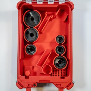 May include: A red tool case with a clear lid, open to reveal various black circular tools of different sizes. The case is designed to hold and organize the tools, with molded compartments. The tools appear to be for electrical work.