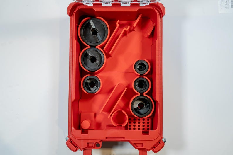 May include: A red tool case with a clear lid, open to reveal various black circular tools of different sizes. The case is designed to hold and organize the tools, with molded compartments. The tools appear to be for electrical work.