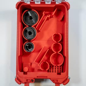 May include: Open red plastic tool case with various black and red tools inside. The case is rectangular with a clear hinged lid. The tools include circular saw blades and other cutting tools. The case is designed for organization and storage.