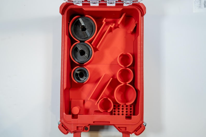 May include: Open red plastic tool case with various black and red tools inside. The case is rectangular with a clear hinged lid. The tools include circular saw blades and other cutting tools. The case is designed for organization and storage.