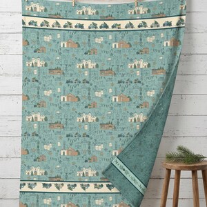 May include: A teal throw blanket featuring a repeating pattern of adobe-style buildings, pine trees, and trucks carrying Christmas trees. The design includes horizontal bands with a row of trucks and a dark teal reverse side with leaf motifs.