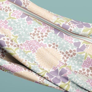 May include: A fabric with a floral pattern in pastel colors. The design features large and small flowers in shades of lavender, peach, and light blue, with green leaves and brown heart-shaped accents. A striped border runs along the edge.