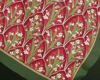May include: A square fabric scarf featuring a repeating pattern of white snowdrop flowers with green leaves set against a deep red background. The design is organised into arched, scale-like segments outlined in white, finished with a solid green border.