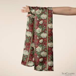 May include: A long rectangular scarf featuring a deep burgundy background with a repeating pattern of cream-colored chrysanthemum flowers and green leaves. The scarf includes vertical green stripes and the text SEACLAIRE copyright 2026.