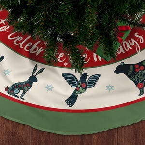 May include: A Christmas tree skirt with a cream background, red border, and green trim. The skirt features illustrations of a rabbit, bird, and bear, with floral accents. The text "Happy to celebrate holidays together" is printed on the red border.