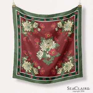 May include: A square scarf featuring a deep red background with a central cluster and four corner arrangements of white chrysanthemums and red flowers. The design is framed by a dark green border with small red floral accents and the text SEACLAIRE.