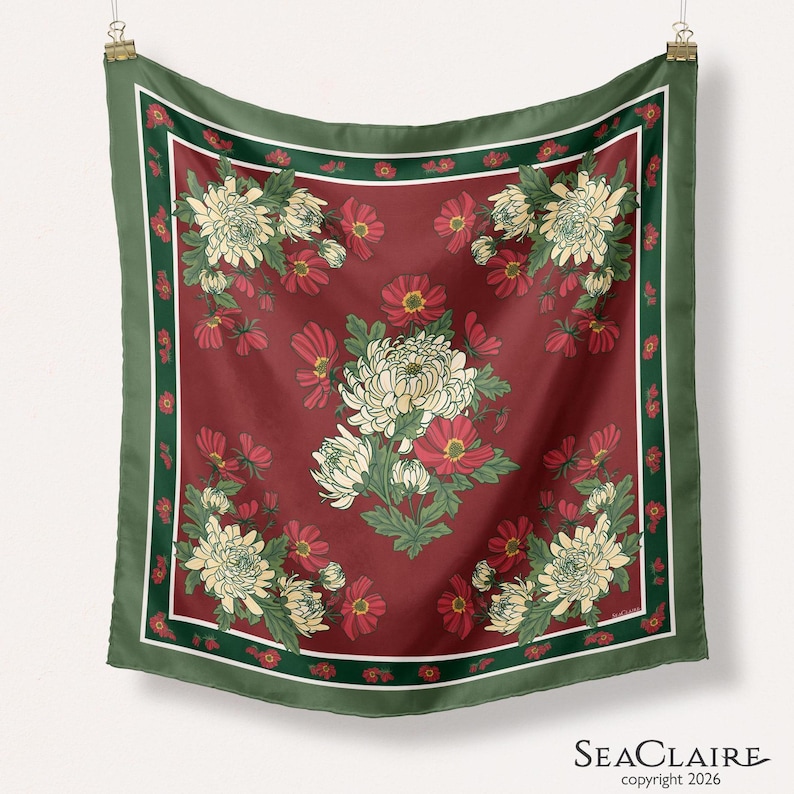 May include: A square scarf featuring a deep red background with a central cluster and four corner arrangements of white chrysanthemums and red flowers. The design is framed by a dark green border with small red floral accents and the text SEACLAIRE.