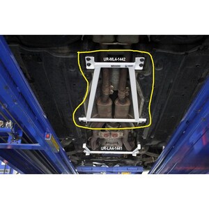 May include: A white metal undercarriage brace bar with the text UR-ML4-1442 installed on the underside of a vehicle. The brace is positioned around the exhaust pipes and is secured with bolts. A second smaller white brace labeled UR-LA4-1441 is visible.