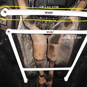 May include: Two white metal automotive chassis reinforcement bars installed under a vehicle. The top bar is labeled UR-LA2-3196 and the bottom trapezoidal bar is labeled UR-ML4-3197. Both bars feature the Ultra Racing brand logo in red and black text.