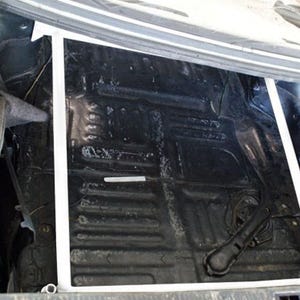 May include: An interior view of a car trunk, showing the floor and side panels. The trunk's interior is primarily black, with some visible metal and a white frame. The trunk appears to be empty.