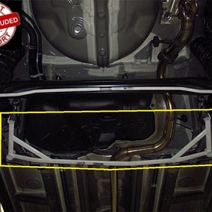 May include: A white metal automotive chassis brace installed underneath a vehicle, featuring a triangular structural design highlighted by a yellow border, positioned near the black fuel tank and metallic exhaust piping system.