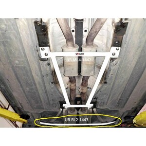 May include: A white metal automotive chassis brace installed under a vehicle, featuring the text UR-ML4-1442 on the main frame and UR-RL2-1443 on the lower bar, which is highlighted by a yellow oval outline against the car's undercarriage.