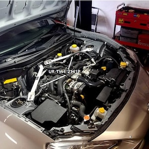 May include: An open car hood revealing the engine compartment. The engine is silver and black, with various components visible, including a strut bar and the text "UR-TW4-2141P". The car's exterior is silver.