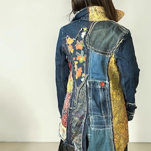 May include: A patchwork jacket constructed from dark blue denim and various floral patterned fabric panels in yellow, orange, and red. The garment features frayed edges, a fold-over collar, and a single visible red button on the back panel.