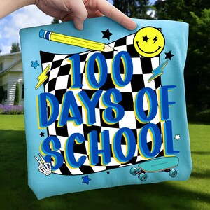 May include: A light blue pillow with the text "100 DAYS OF SCHOOL" in blue and yellow. The design includes a checkered flag, a yellow pencil, a smiley face, lightning bolts, stars, a peace sign, and a skateboard.