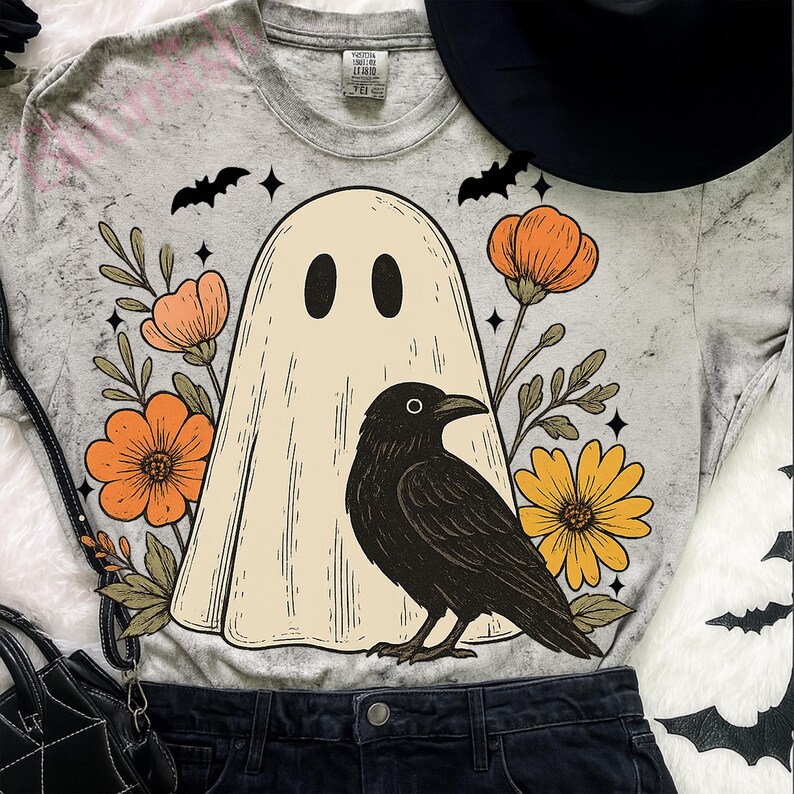 May include: A gray t-shirt featuring a ghost design with a black raven, orange flowers, and yellow flowers. The ghost has two black oval eyes. The shirt also has black bats and stars.