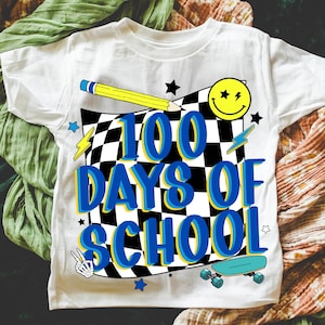 May include: White t-shirt with a colorful graphic design celebrating 100 days of school. The design includes a checkered background, a yellow pencil, a smiley face, stars, lightning bolts, a skateboard, and the text "100 DAYS OF SCHOOL".