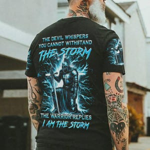 May include: Black t-shirt with a graphic of a knight kneeling in a storm, with the text "THE DEVIL WHISPERS YOU CANNOT WITHSTAND THE STORM" and "THE WARRIOR REPLIES I AM THE STORM" in blue.