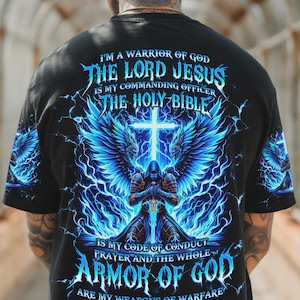 Könnte beinhalten: Schwarzes T-Shirt mit einem grafischen Design, das ein Kreuz, Engelsflügel und eine Kapuzenfigur zeigt. Der Text enthält "I'M A WARRIOR OF GOD", "THE LORD JESUS" und "ARMOR OF GOD" in einem blau-weißen Farbschema. Das Design enthält Blitzelemente.