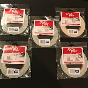 May include: Five rolls of Scor-Tape double-sided adhesive tape, each in a clear plastic package. The tape rolls are 1/4 inch wide and 27 yards long. The packaging includes the text "Scor-Tape" and details about its use for crafts.