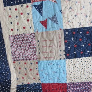 May include: A patchwork quilt with a patriotic theme. The quilt features squares of blue, red, and white fabrics with star, flag, and geometric patterns. Some squares have the text "Thank you!". The quilt is bordered with a blue fabric with white stars.