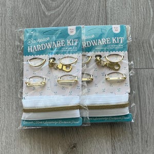 May include: Two packages of backpack hardware kits. Each kit includes gold-colored metal hardware pieces, white elastic, and a gold-colored zipper. The packaging is teal and white with the text "Backpack Hardware Kit."
