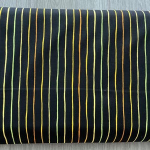 May include: Black fabric with vertical stripes in yellow, orange, and green. The stripes are evenly spaced and run the length of the fabric. The fabric appears to be folded over.