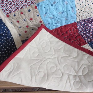 May include: A patchwork quilt with a patriotic theme, featuring red, white, and blue fabrics. The quilt showcases star and flag patterns, with a red border. The underside is white with star-shaped quilting.