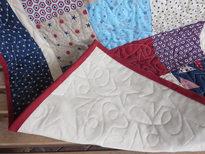 May include: A patchwork quilt with a patriotic theme, featuring red, white, and blue fabrics. The quilt showcases star and flag patterns, with a red border. The underside is white with star-shaped quilting.