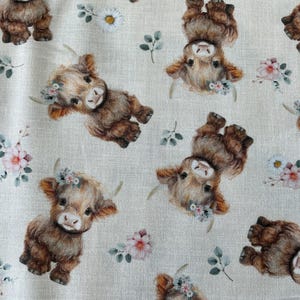 May include: Fabric with a repeating pattern of brown Highland cows wearing floral crowns. The cows are interspersed with watercolor-style flowers in pink, white, and green, set against a light beige background.