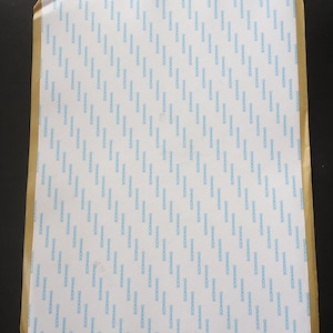 May include: A sheet of white paper with a repeating pattern of the word "SOOKWANG" in blue. The paper has a light brown border and is likely used for packaging or wrapping.