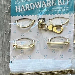 May include: A package of backpack hardware kit with gold-colored metal pieces, including buckles and a zipper pull. The package is labeled "Backpack Hardware Kit" with the text "Riley Blake Designs" and "with Minki Kim".