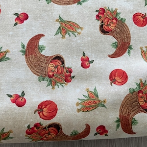 May include: A beige fabric with a repeating pattern of autumn harvest elements. The design includes cornucopias filled with pumpkins and apples, along with individual pumpkins, apples, and ears of corn. The overall color palette is warm, featuring shades of red, orange, and brown.