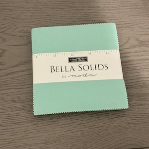 May include: A light blue fabric square with the text "Bella Solids by moda" printed on a white label.