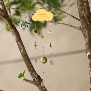 以下が含まれることがあります： さまざまな形とサイズのぶら下がっているチャームが付いた、金色の雲型の風鈴。雲には「Forever my best friend. Listen to the wind and know Lancaster.」というテキストがあります。