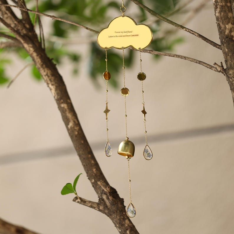 以下が含まれることがあります： 雲の形をしたトップとぶら下がっているチャームが付いた、金色の風鈴。チャームには、ビーズ、星、しずく型のペンダントが含まれます。雲には「Forever my best friend. Listen to the wind and know I am near.」と書かれています。