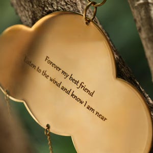 以下が含まれることがあります： 「Forever my best friend. Listen to the wind and know I am near.」と刻まれた、金色の雲型のウィンドチャイム。木の枝から吊り下げられています。