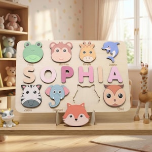May include: A wooden puzzle spelling "SOPHIA" with colourful letters. The puzzle includes animal shapes such as a frog, monkey, giraffe, dolphin, zebra, elephant, fox, and owl. The puzzle is designed for children.