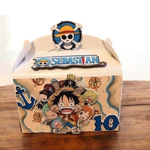May include: A white party favor box featuring a cartoon illustration of characters. The box has a blue anchor, the name "SEBASTIAN" and the number "10". A skull and crossbones logo is on top.
