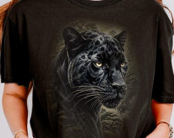 May include: Black t-shirt featuring a detailed illustration of a black panther with yellow eyes. The panther is set against a backdrop of foliage, creating a striking contrast. The shirt has short sleeves and a relaxed fit, suitable for casual wear.