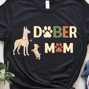 Könnte beinhalten: Eine weiße Keramik-Tasse mit schwarzem Henkel und dem Text "But First, Coffee" in handschriftlichem Stil. Die Tasse steht auf einer weißen Oberfläche. Die Tasse ist etwa 10 cm hoch.